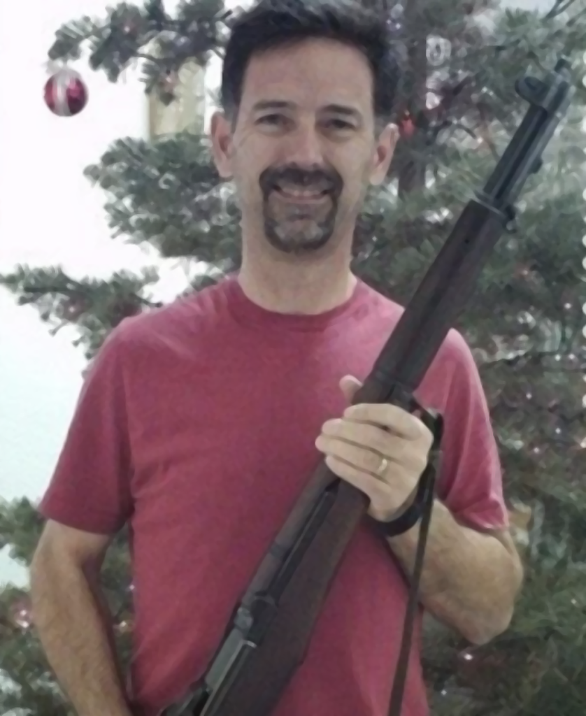 Smiling man, brown hair, red shirt, holding an M1 Garand.