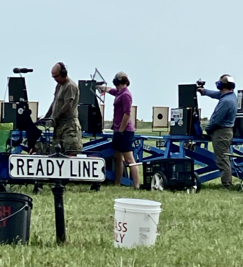 Girl in a purple shirt holding a pistol pointed at a paper target at the National Matches competing. 