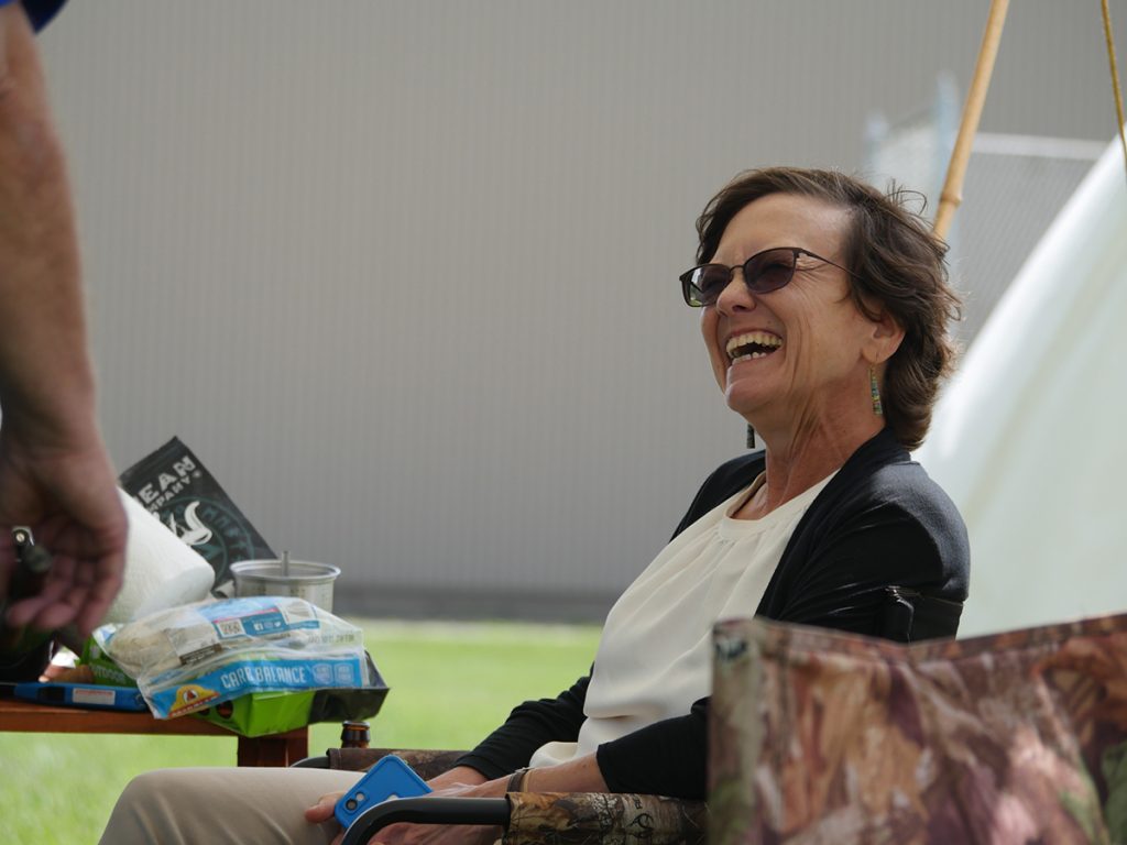 Woman laughing and smiling sitting in a chair with sunglasses on outside of a tent.