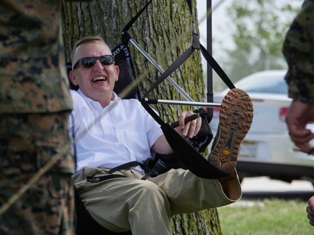 Chair swing hanging from a tree with man sitting in it.