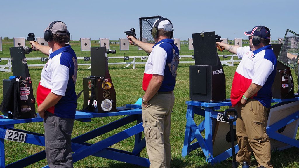 A team of pistol shooters in red, white and blue shirts and brown pants shoot at targets.