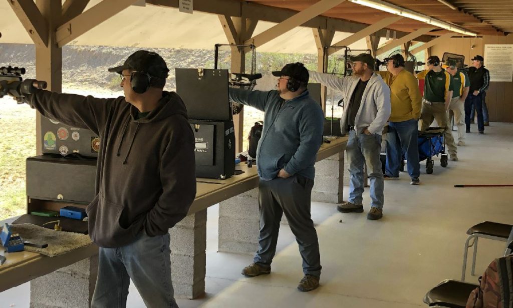 A line of pistol shooters compete at an indoor range.