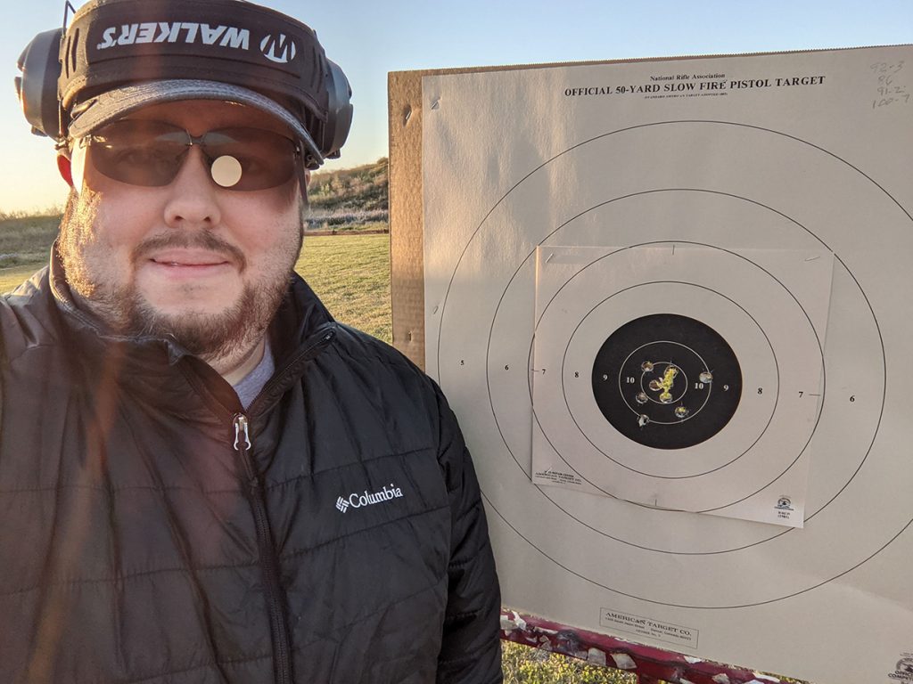 Pistol athlete standing proudly next to his target after a string of good shots.