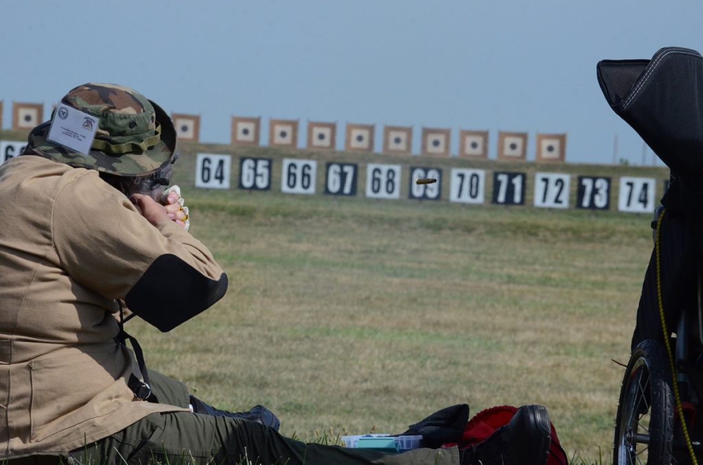 A man aims a rifle downrange in the sitting position.