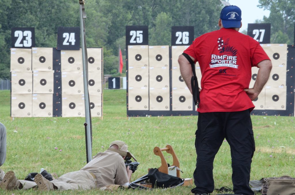 Rex standing on the firing line next a competitor shooting in the prone position during a rimfire sporter match.