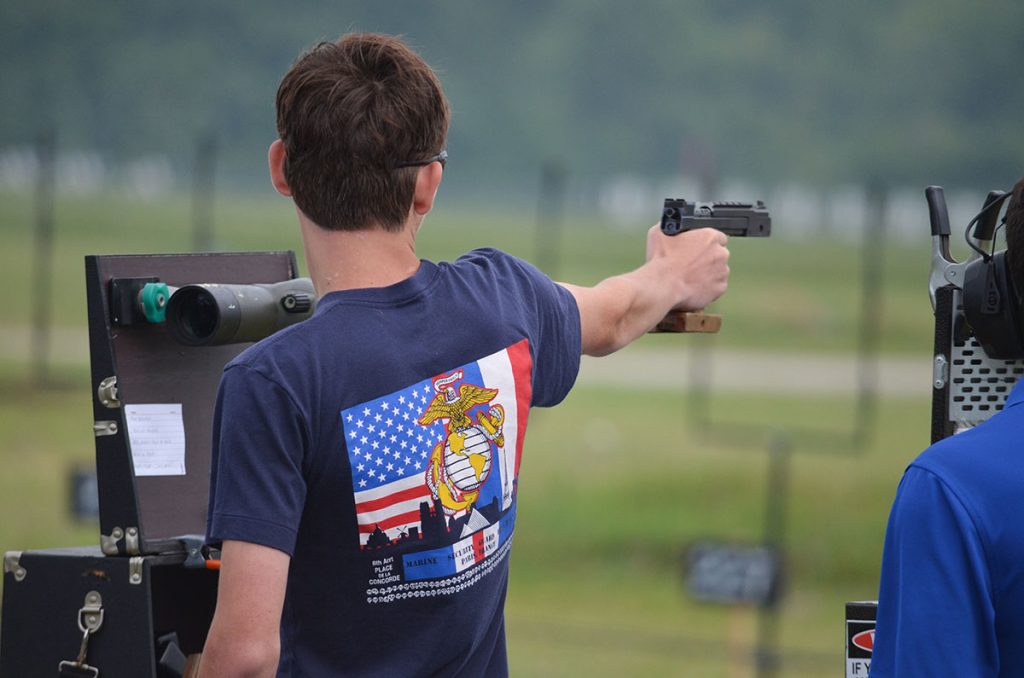 Caleb as viewed from behind, aiming a pistol downrange during the Small Arms Firing School.