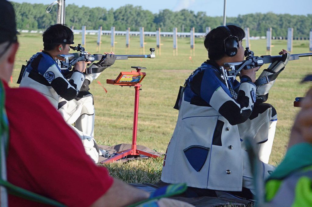 Ryan and Tyler competing next to each other in an outdoor smallbore match. They are both in the kneeling position, aiming downrange.