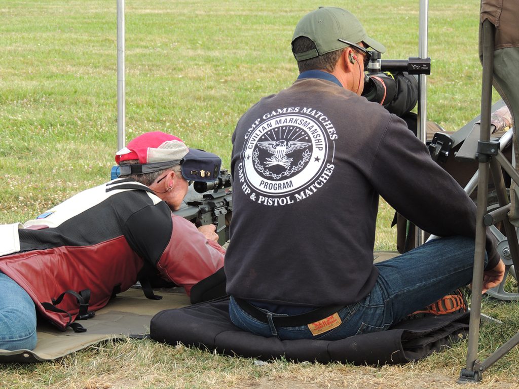A man laying in the prone position with an instructor seated on the ground next to him.