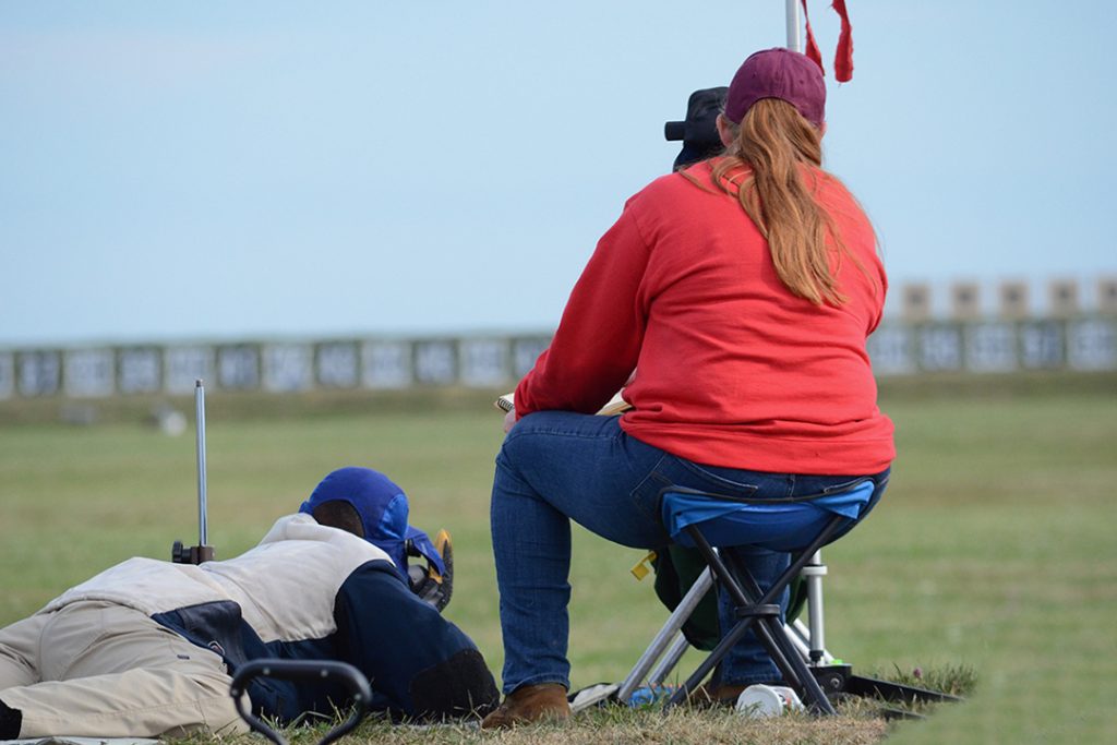 An instructor looking through a scope while a man aims a rifle in the prone position.