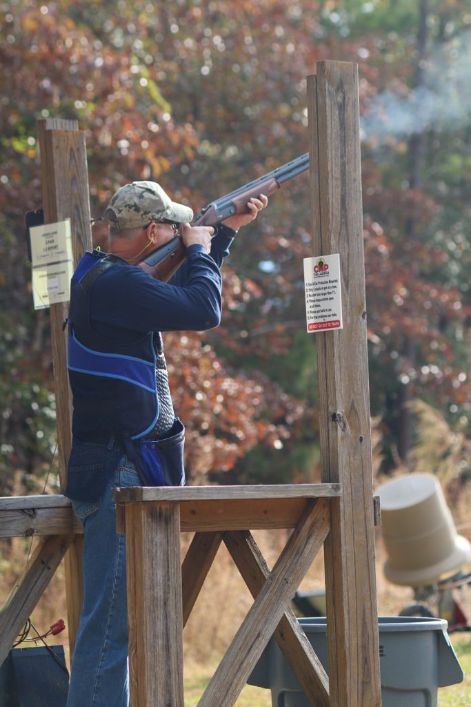 A man firing a shotgun in a sporting clays station.