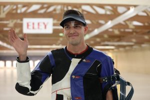 Timothy Sherry in the United States Olympic and Paralympic Training Center rifle range. He is smiling and waving.