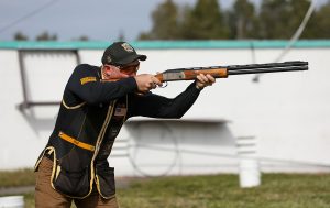 Dustin Taylor aiming a shotgun outside during a skeet event.