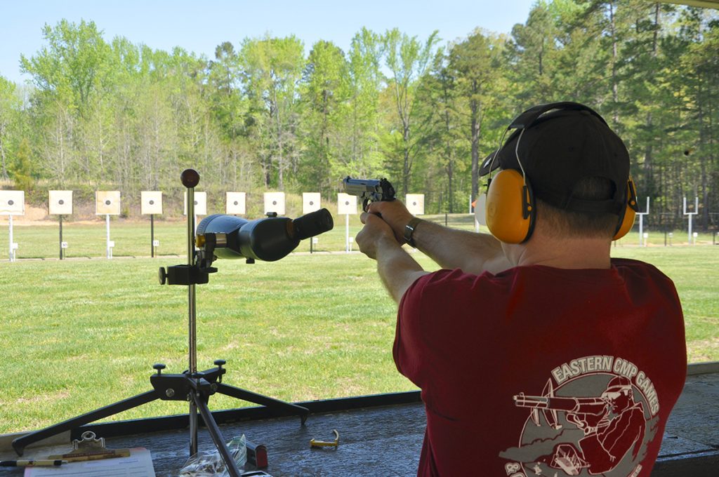 A man firing a pistol outdoors at a target downrange.