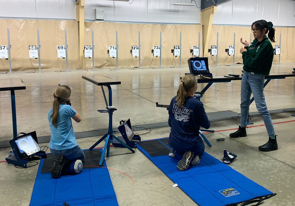 Alana Kelly working with two young sporter shooters who are in the kneeling position.