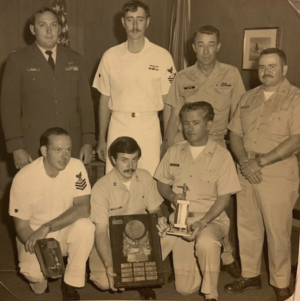 A sepia toned photograph of the Otis Air Force Base combined pistol team. Four men are standing in the back row and three men are kneeling in the front with trophies.
