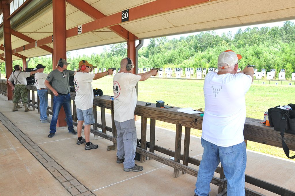 Pistol competitors on the firing line, aiming downrange.