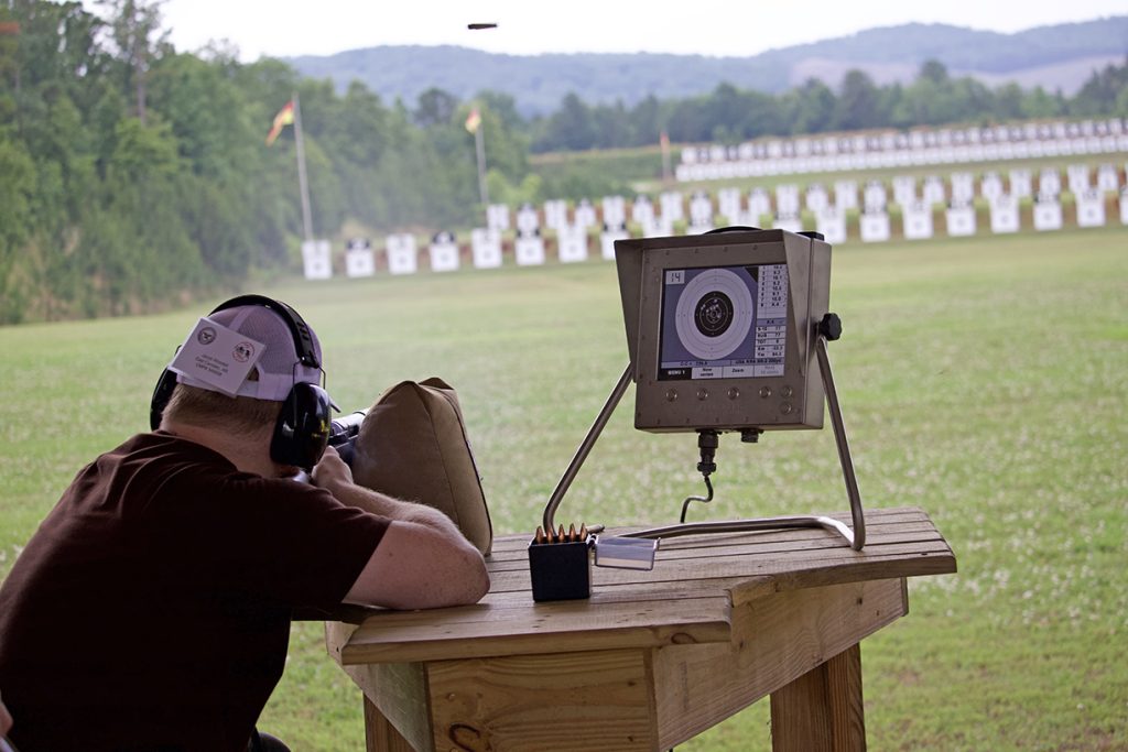 A competitor aiming a rifle downrange at the electronic targets.