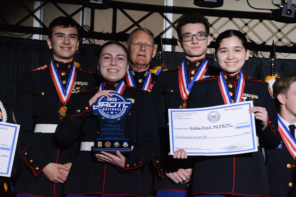 Nation Ford High School on the podium, posing with their medals, trophy, and check prize.