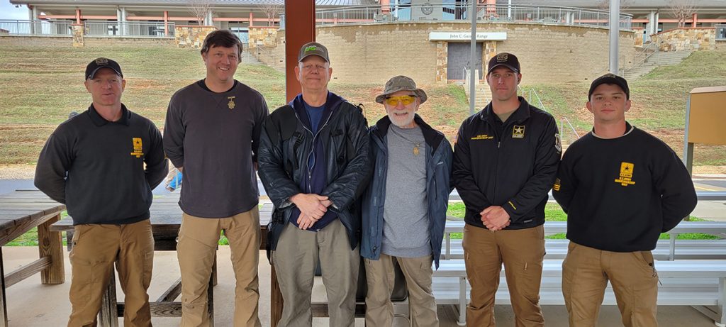 Three competitors standing together with members of the U.S. Army Marksmanship Unit on the range. The are all facing the camera.