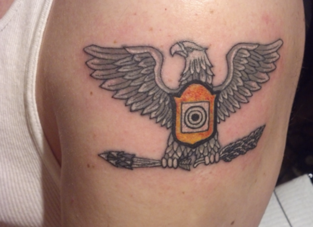Doc's tattoo of the Distinguished Pistol Shot badge. The badge has replaced the shield in front of a Colonel's eagle with it's wings spread out.