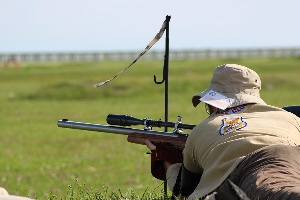 Long range athlete in a brown jacket and bucket hat wait for their commands as the wind blows their flag to let them know direction. 