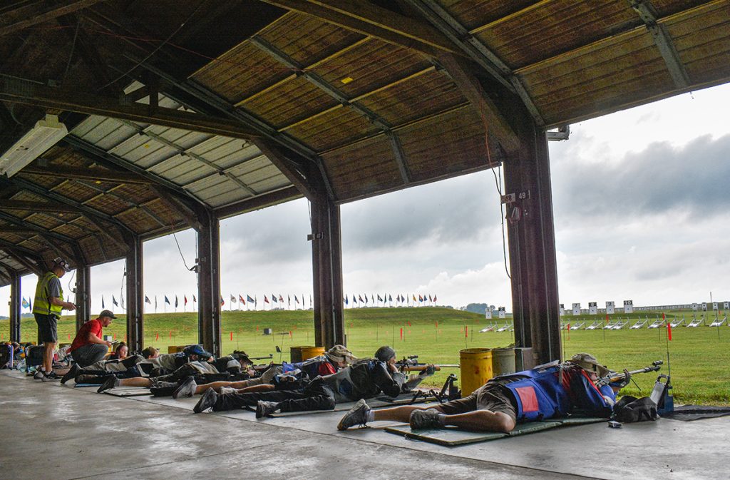 Smallbore firing line with competitors in prone firing at electronic targets.