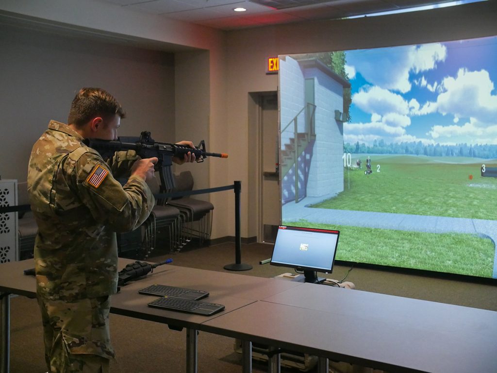 Marksman aiming at simulator screen with rifle.