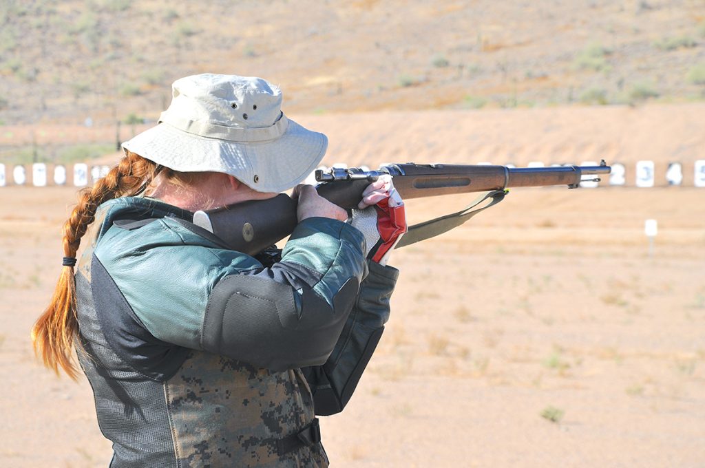 Julia Carlson standing outside, aiming a rifle downrange.