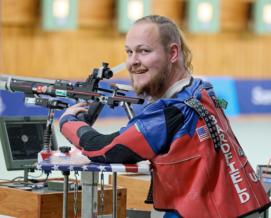 Stetson Bardfield during an air rifle competition. He is looking back at the camera and smiling.
